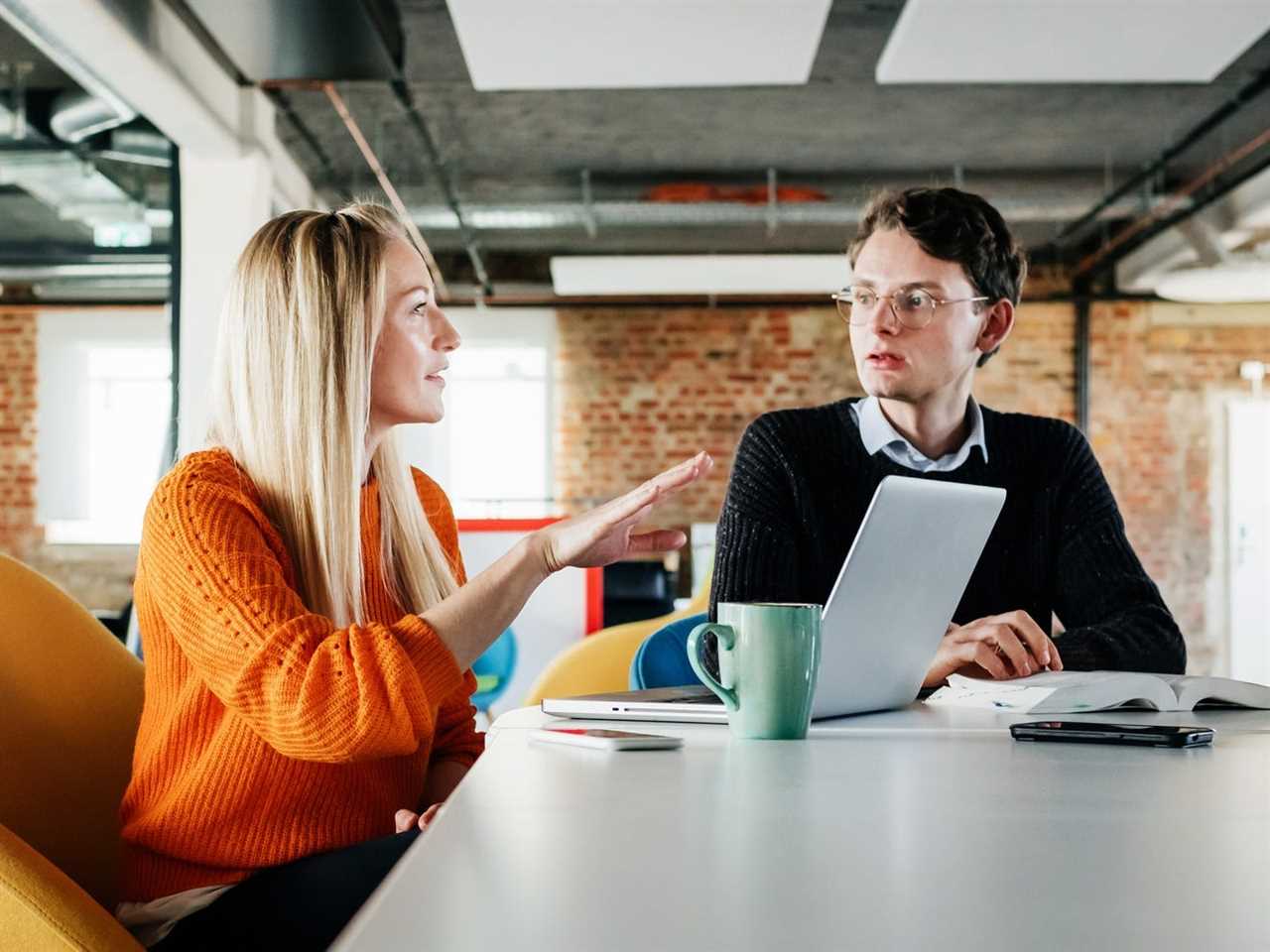 Two business colleagues discussing a technical problem at their desk in a modern office space.