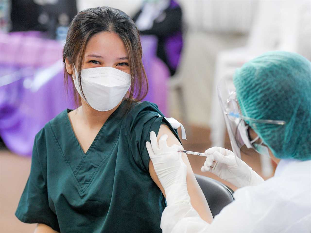 healthcare worker in mask, smiling, getting booster shot.