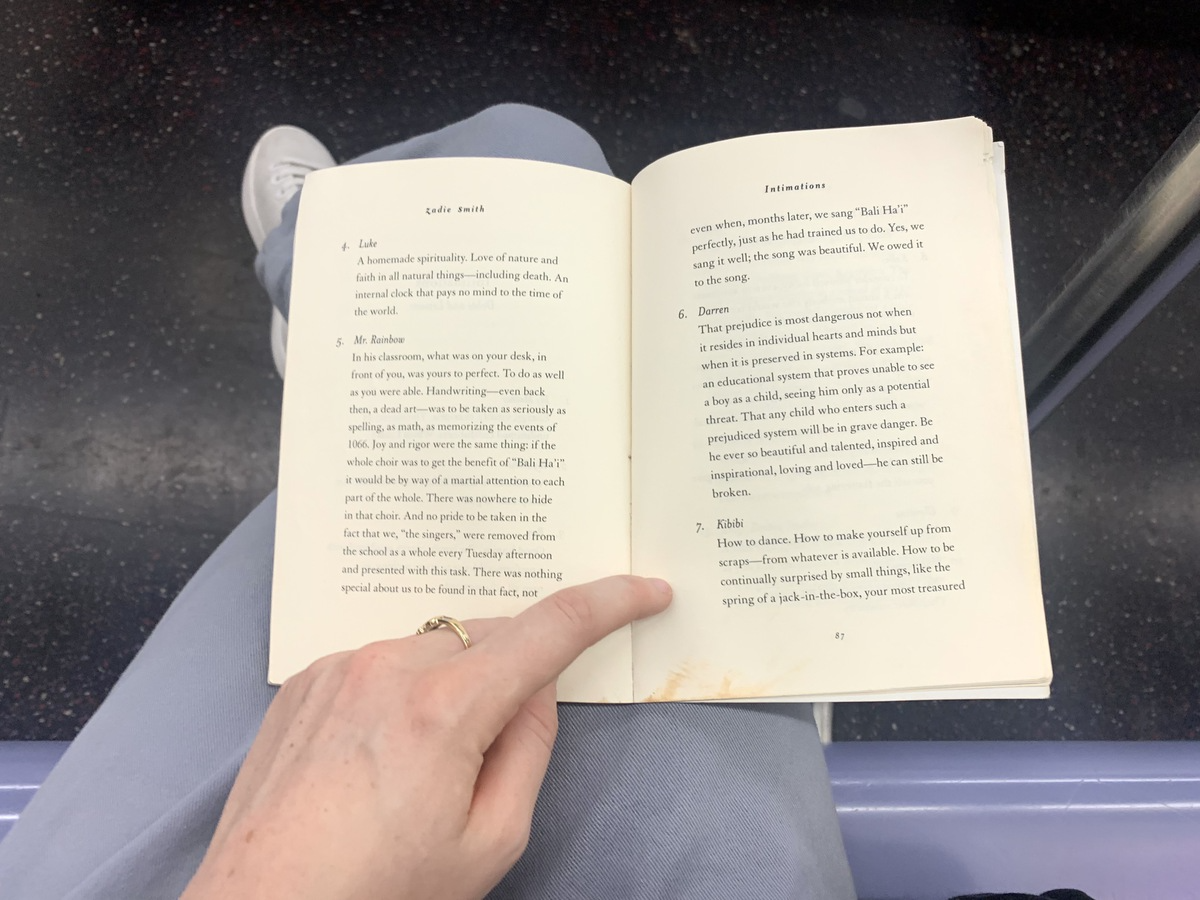 "Intimations" by Zadie Smith open, resting on author's legs on the subway