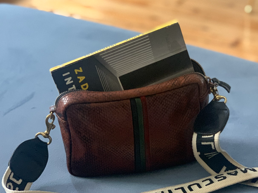A photo of a snakeskin bag with “Intimations” inside of it