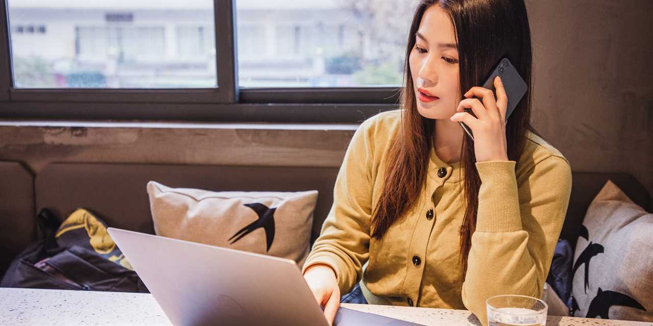 Woman in a yellow sweater talking on her phone in front of a computer