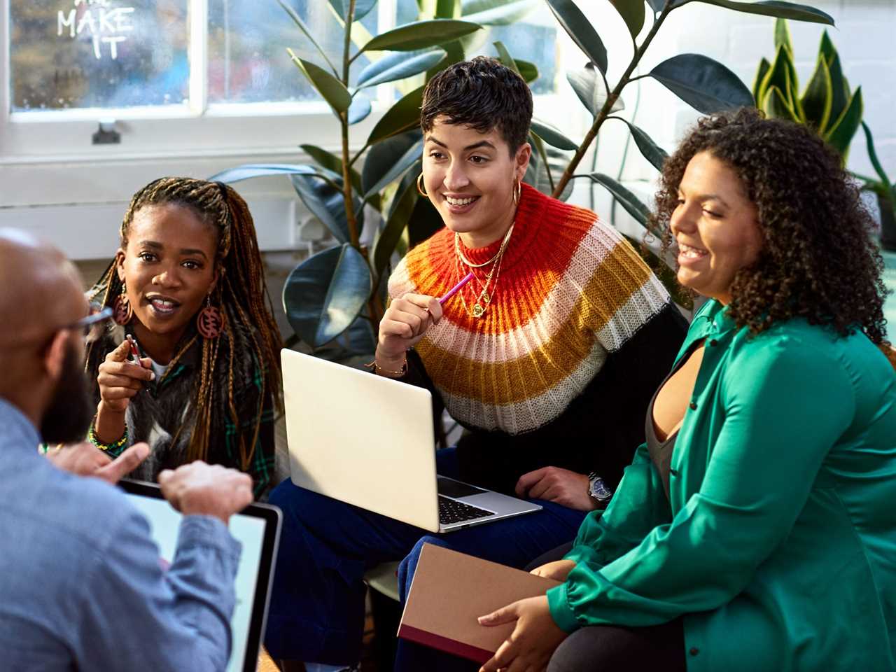 Four people sit together with their laptops and books discussing something exciting