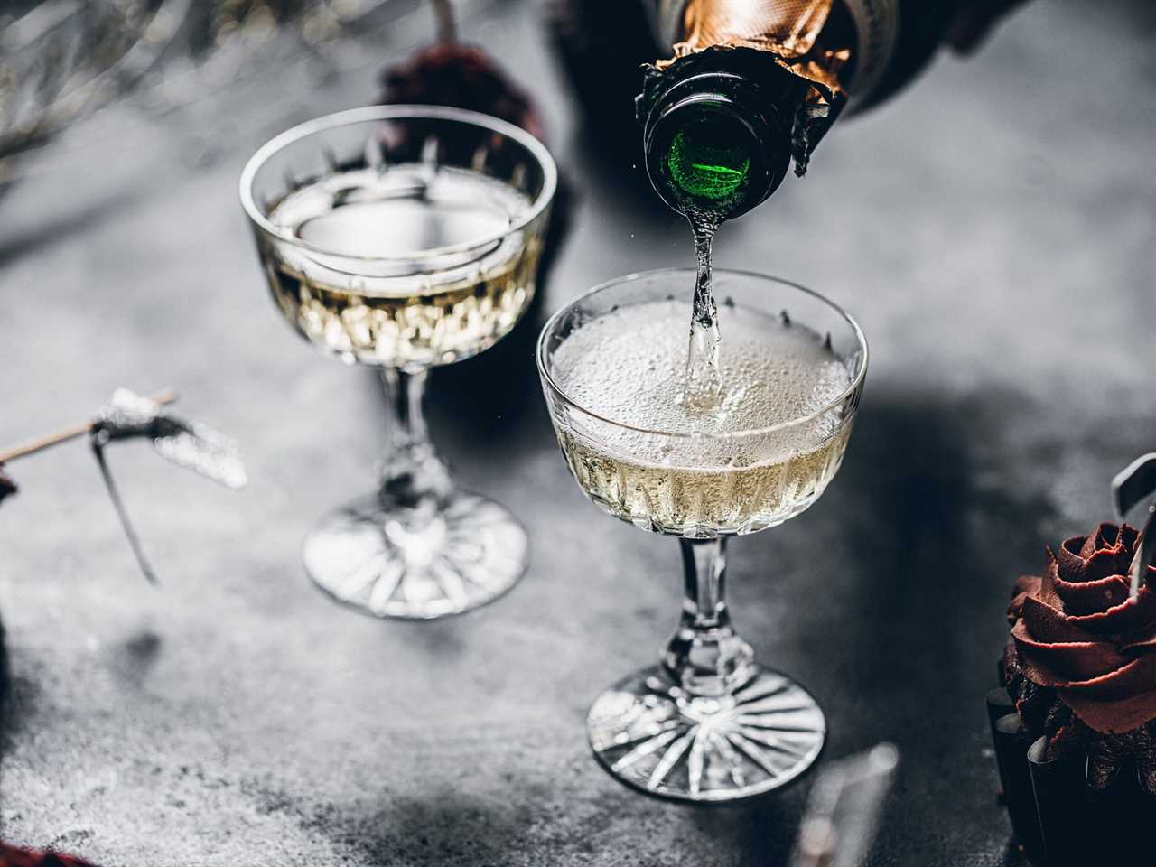 A bottle of champagne being poured into two coupe glasses